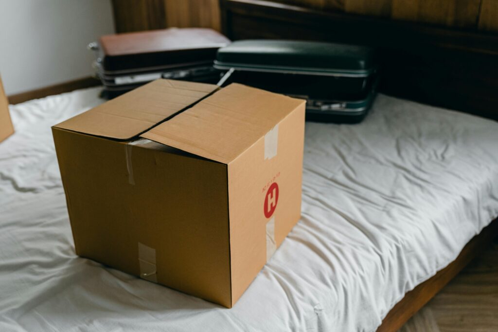 A carton and luggage on a bed in the concept of moving to Leyton