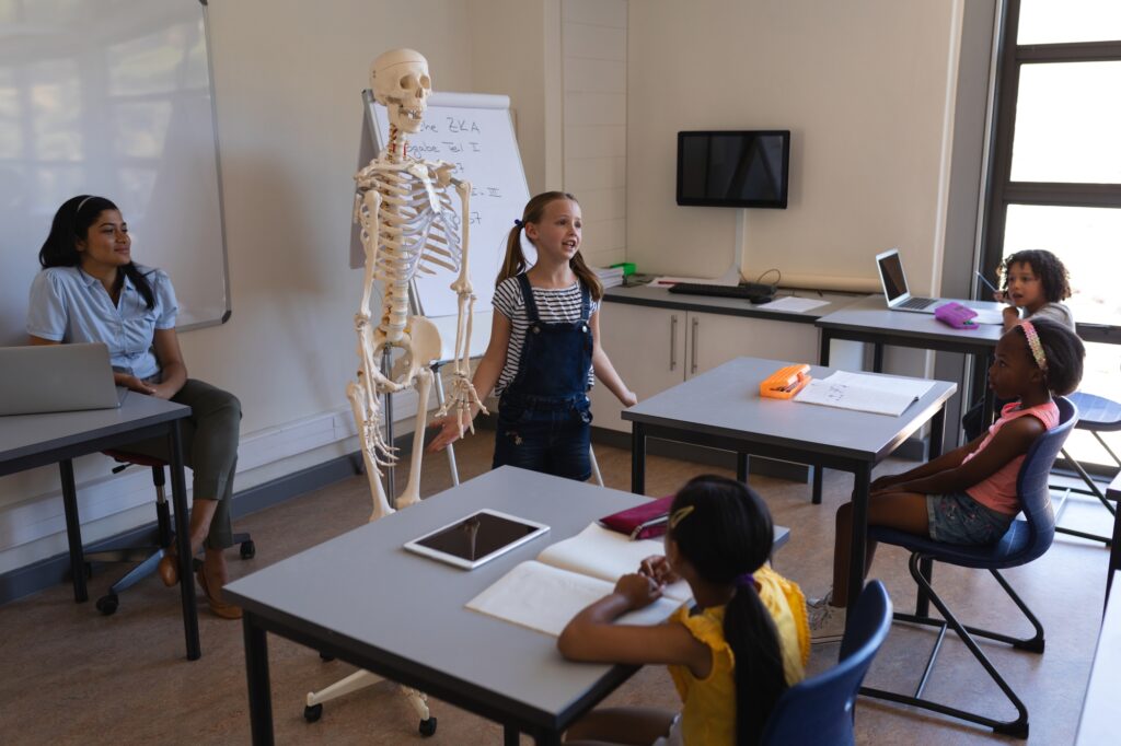 A student in front of the class is sharing her knowledge about the human skeleton.