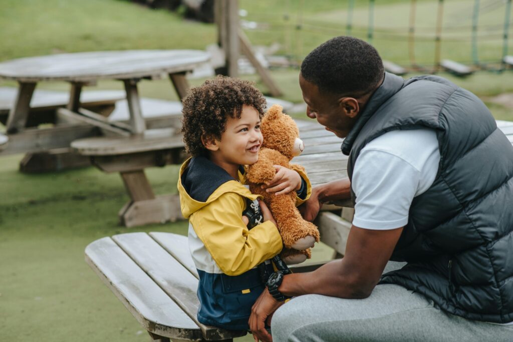 A father and son at a park sitting on a wooden bench in the concept of amenities in Leyton for new residents.